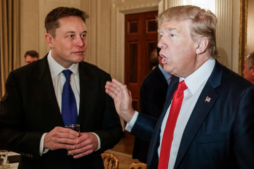 Donald Trump speaking at a rally with Elon Musk in the background.